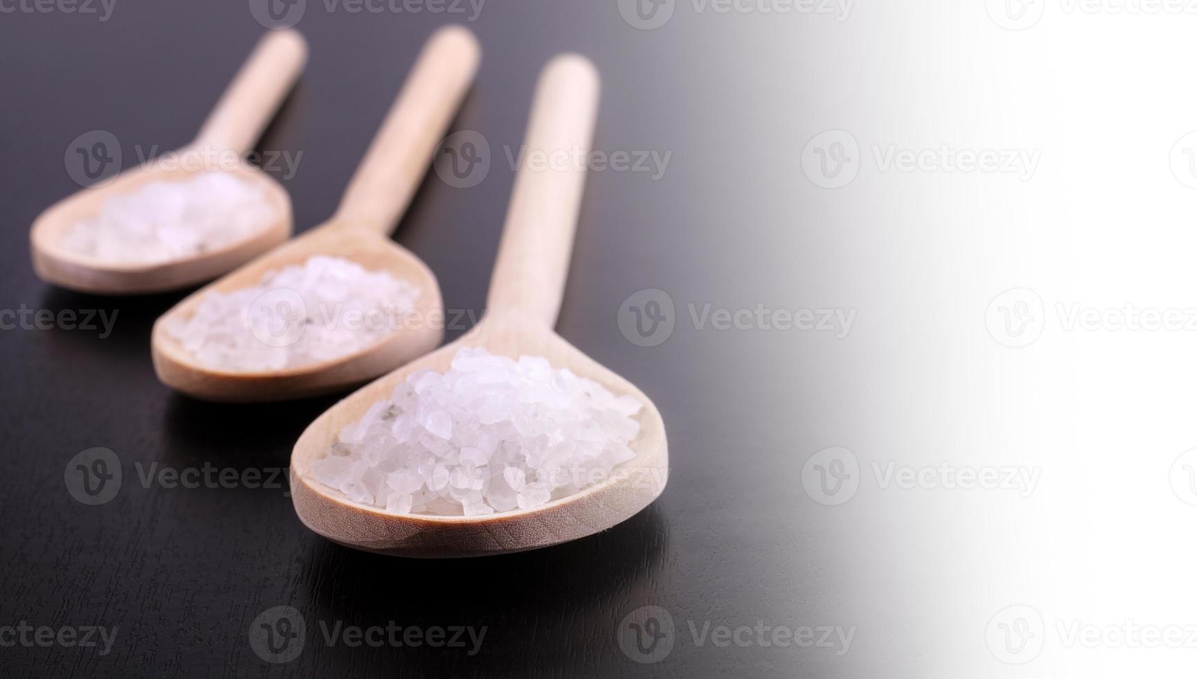 Bath salt in three wooden spoons on a dark polished desk in backlight photo