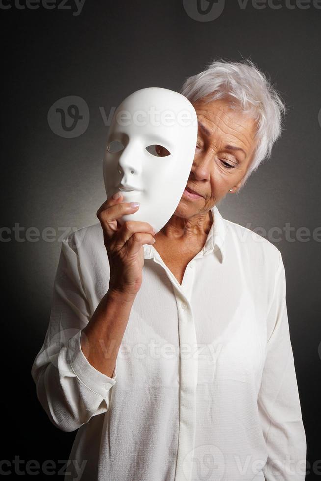 mujer madura que valora la cara triste detrás de la máscara foto