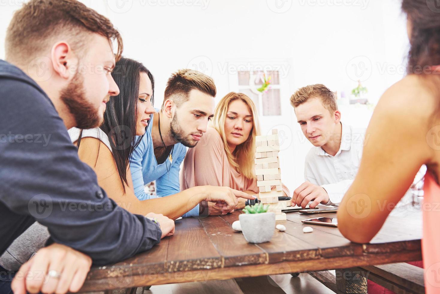 grupo de amigos creativos sentados en la mesa de madera. gente divirtiéndose mientras juega al juego de mesa. foto