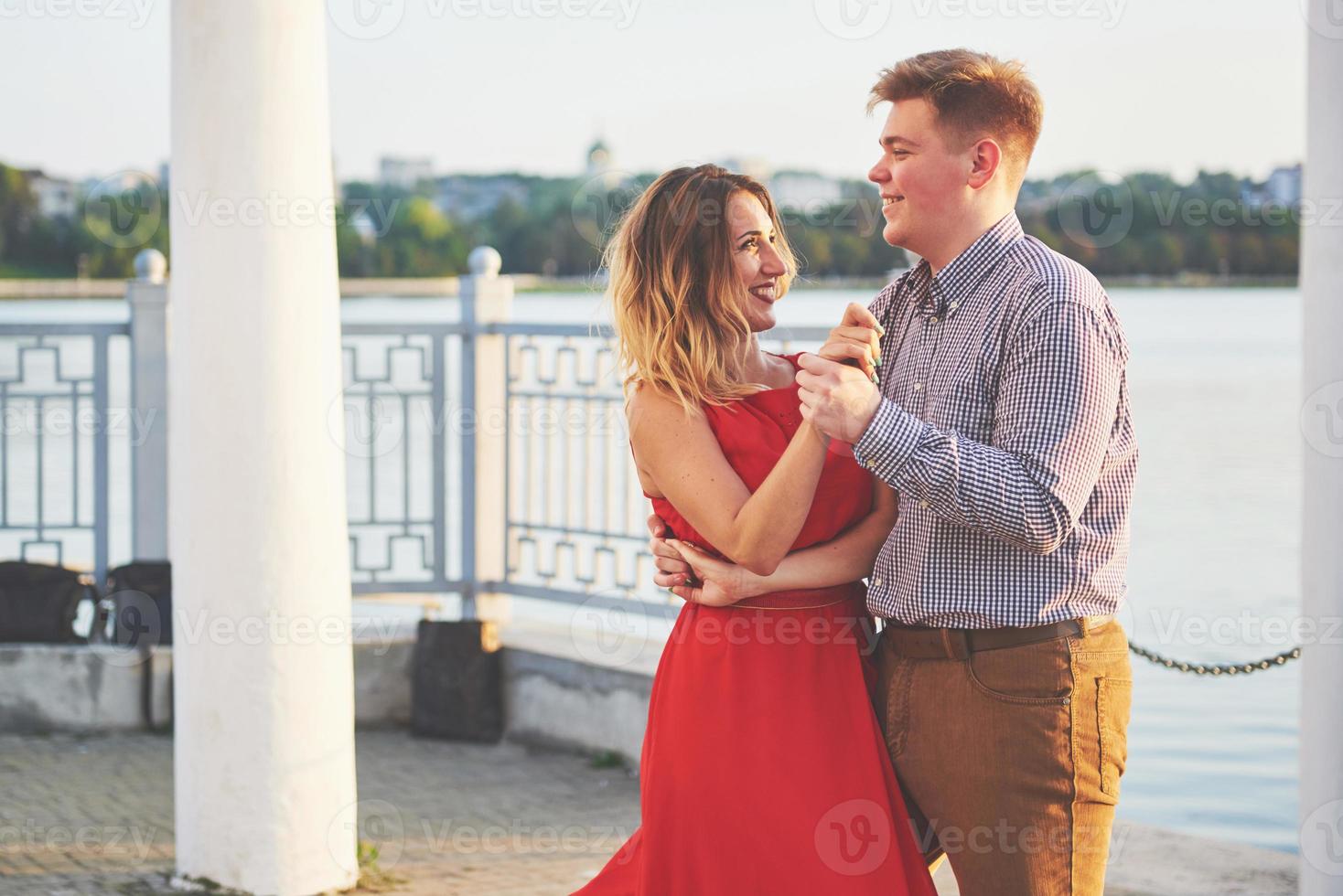 Happy beautiful woman in red dress and young man dance of on summer with lake in the background. Color contrast red and white photo
