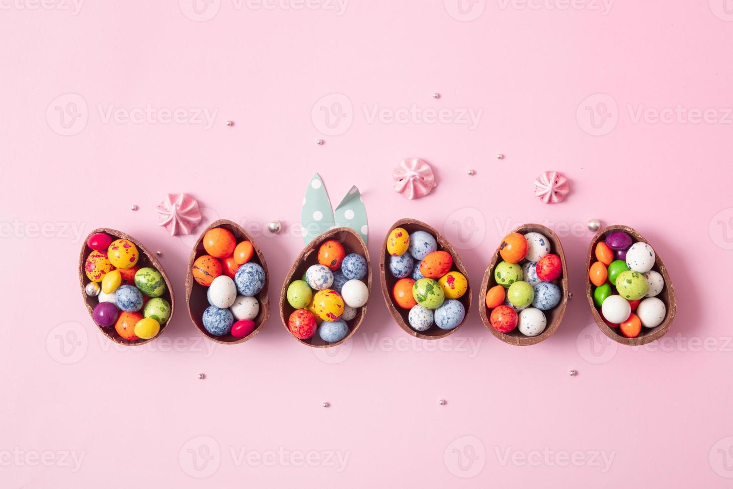 Chocolate easter eggs and decor flat lay for kids easter hunt egg concept on pink background. Sweets in the shape of an egg photo