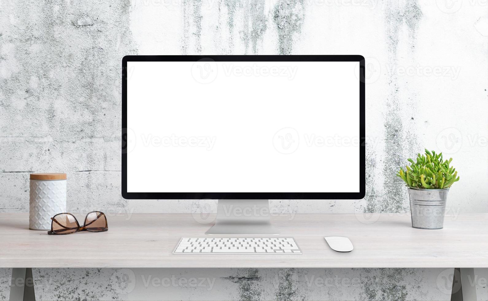 pantalla de computadora en el escritorio de la oficina con pantalla aislada para maqueta, presentación de página wep. escritorio limpio con planta, vasos y caja. pared rugosa blanca en el fondo foto