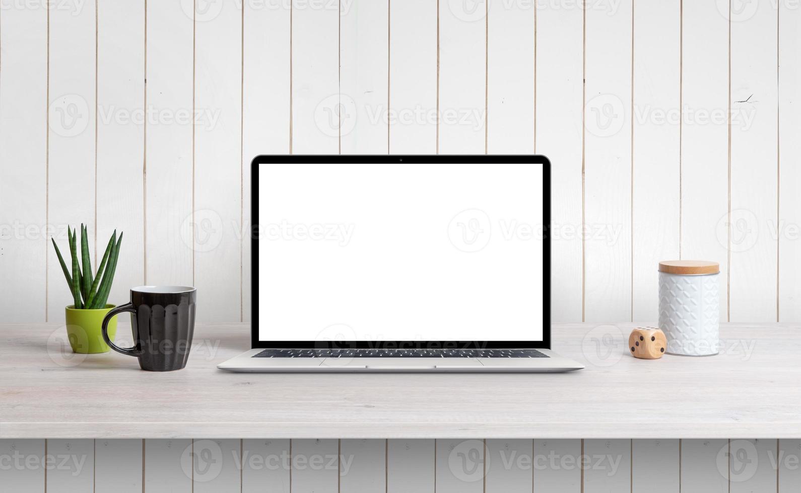 Lapop on desk with isolated white screen for mockup, app or web page design promotion. White wooden wall in background photo