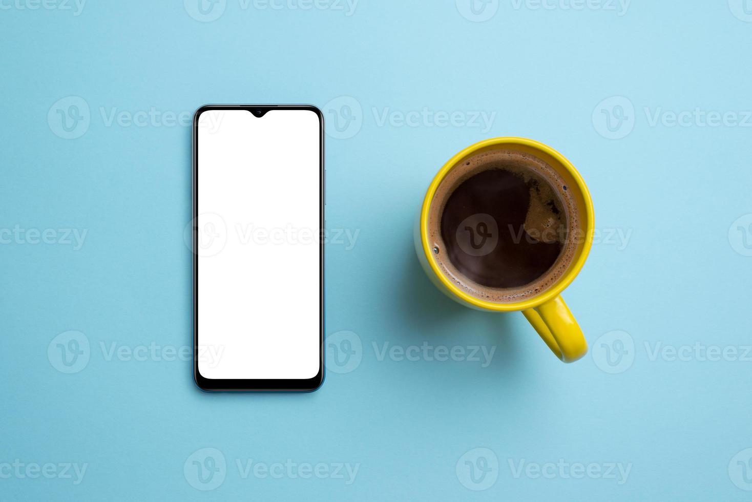 Phone mockup and coffee mug on clean blue surface. Top view, flat lay composition. Smart phone with blank, white isolated screen for app presentation photo