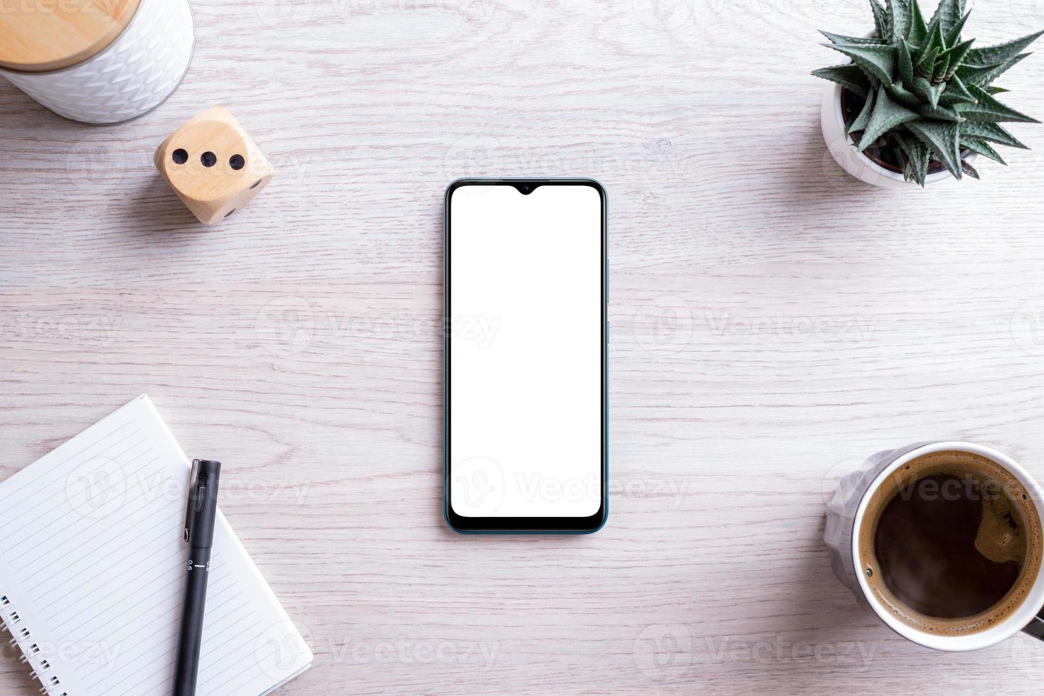 Flat lay phone mockup composition on work desk. Isolated screen for app presentation. Pad with pen, coffee mug, plant and box beside. Clean office desk photo