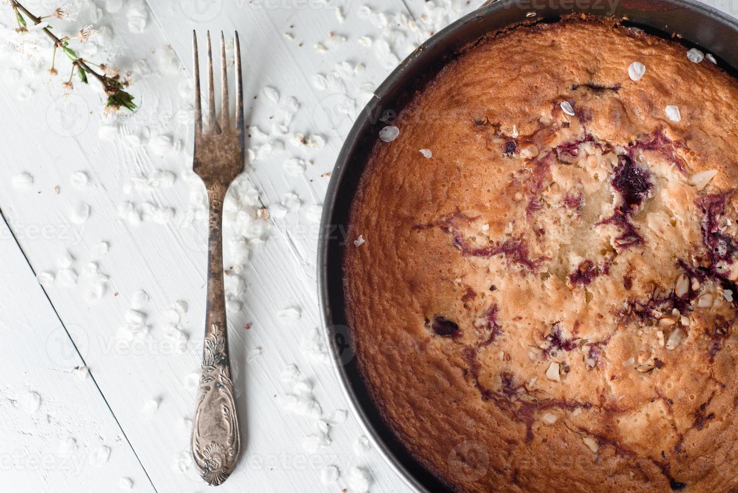 tarta de cerezas sobre un fondo blanco de madera. cerca hay una vieja cuchara de plata y flores de primavera. foto