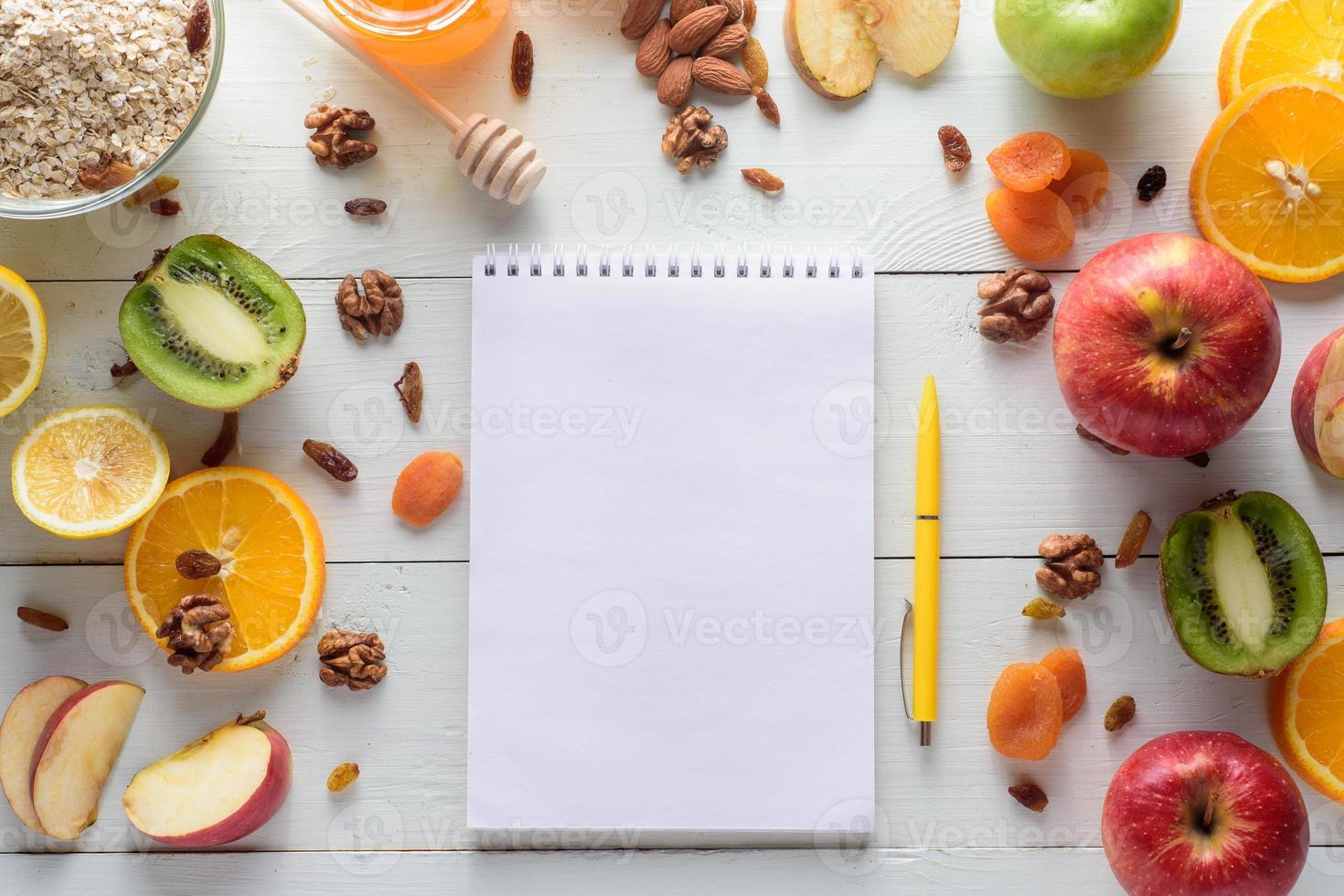 Notebook with pen surrounded by apples, kiwi, dried fruits, oranges and apples. The concept of a healthy diet and shopping list. photo