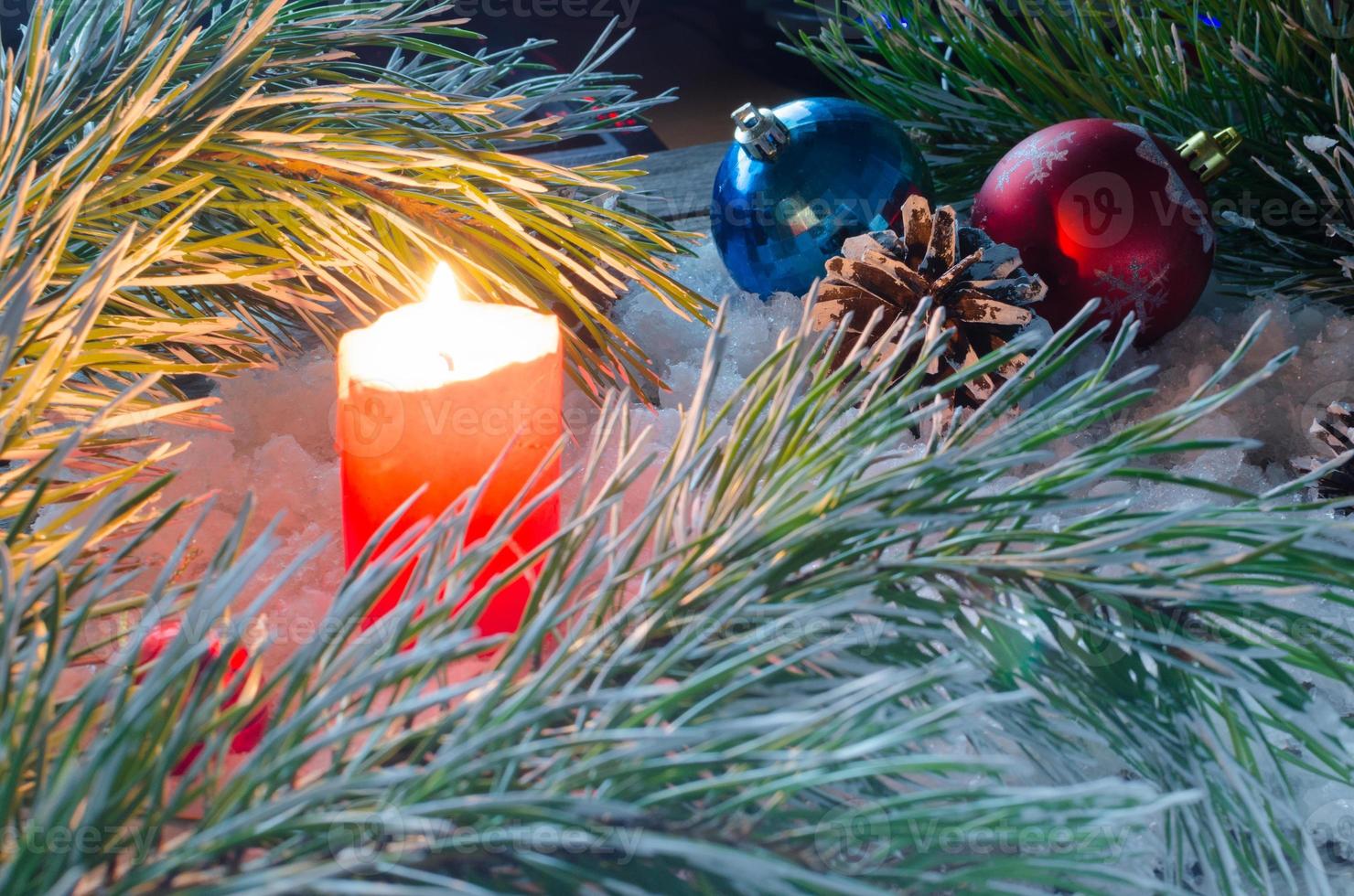 Burning candle on the snow among the branches of spruce and toys for Christmas photo