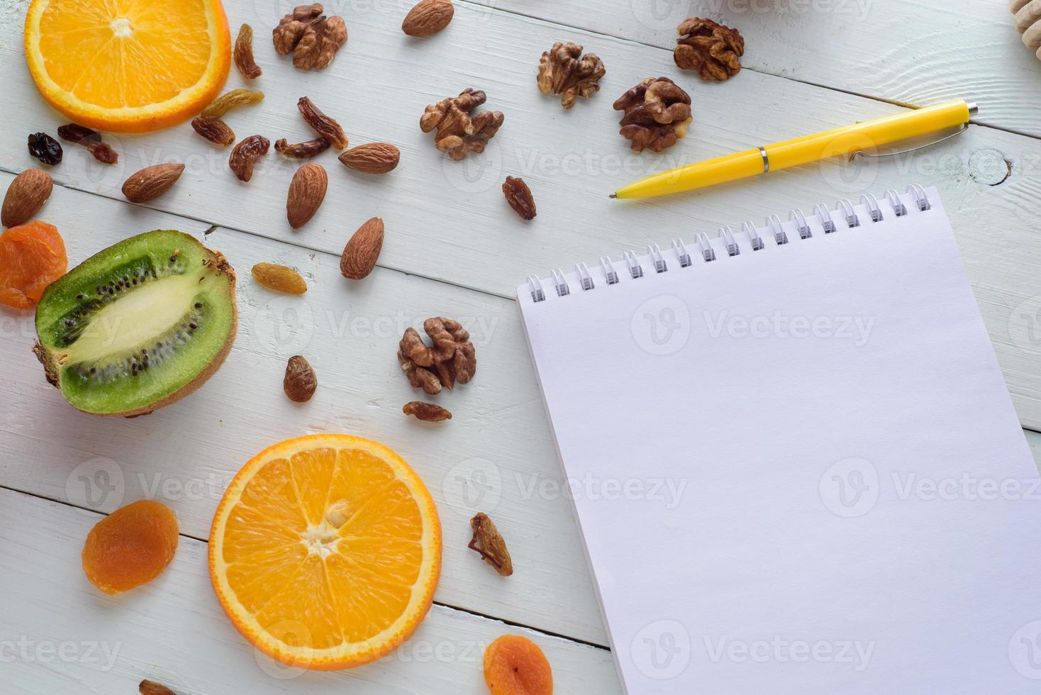 cuaderno con bolígrafo rodeado de manzanas, kiwi, frutos secos, naranjas y manzanas. el concepto de una dieta saludable y una lista de compras. foto