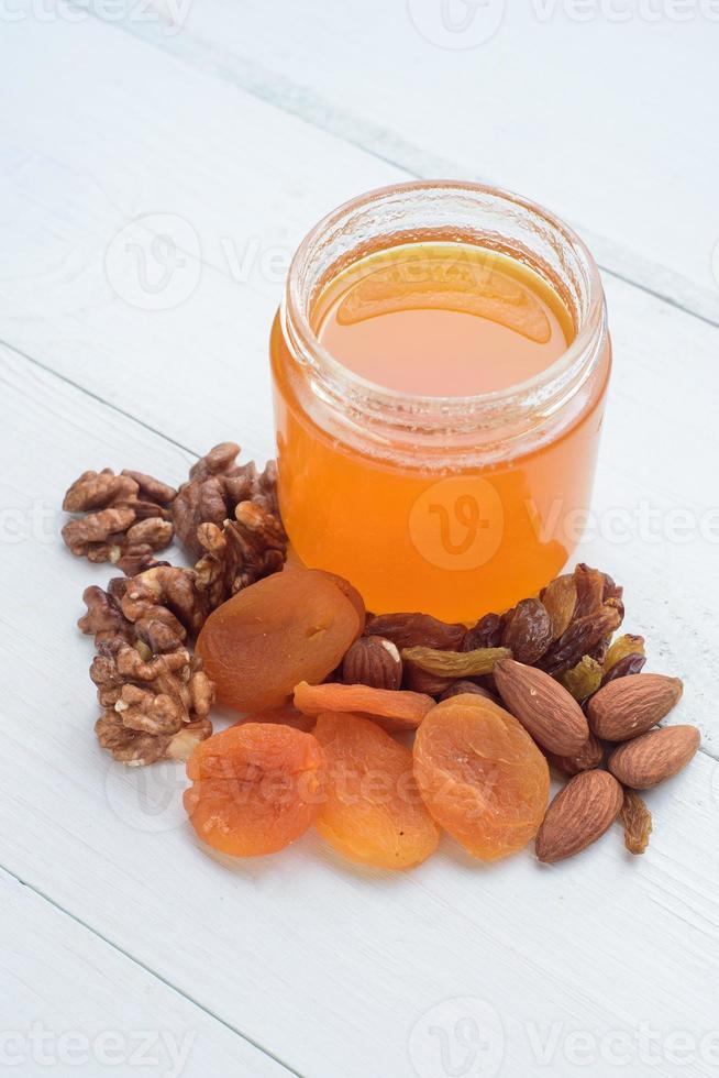 miel, almendras, nueces y albaricoques secos. frutas secas sobre una mesa de madera blanca. foto