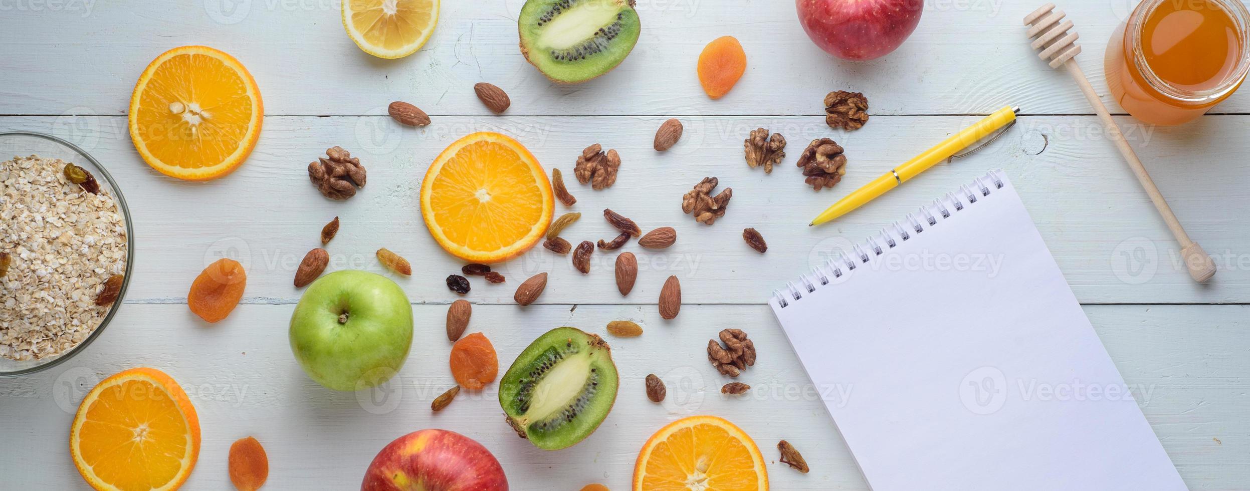 Notebook with pen surrounded by apples, kiwi, dried fruits, oranges and apples. The concept of a healthy diet and shopping list. photo