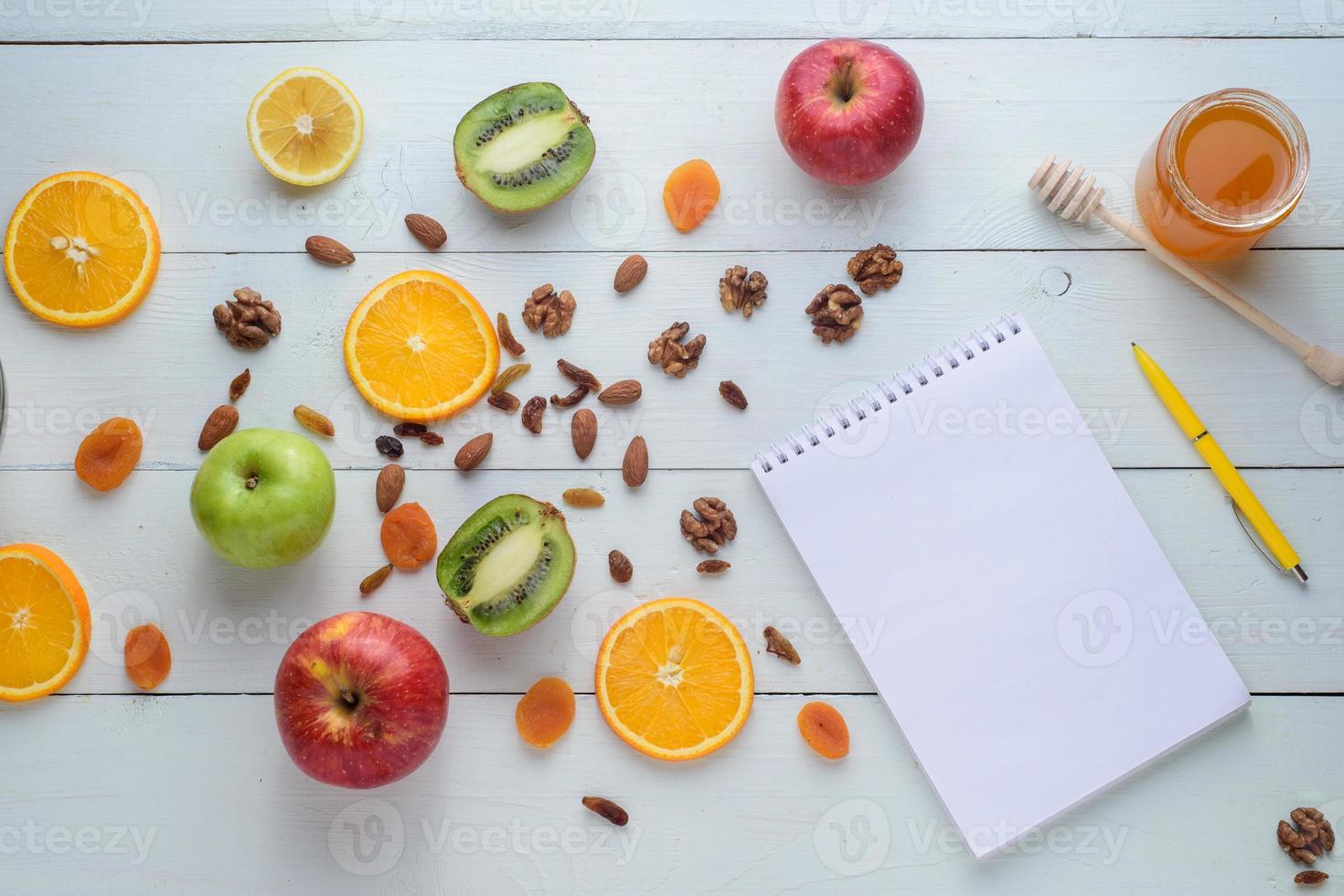 Notebook with pen surrounded by apples, kiwi, dried fruits, oranges and apples. The concept of a healthy diet and shopping list. photo