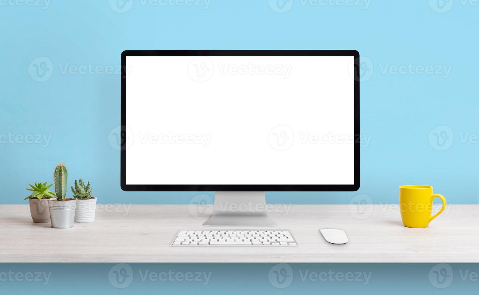 Computer display with white isolated screen for presentation on work desk. Clean composition with coffee mug and plants. Blue wall in background photo