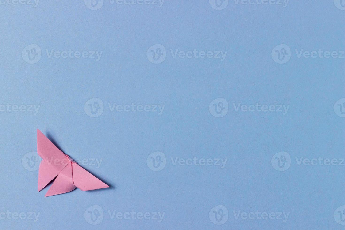 Pink origami butterfly folds out of paper. Blue background with copy space. Education, pastime, hobbies, activities with children. Minimalistic background photo