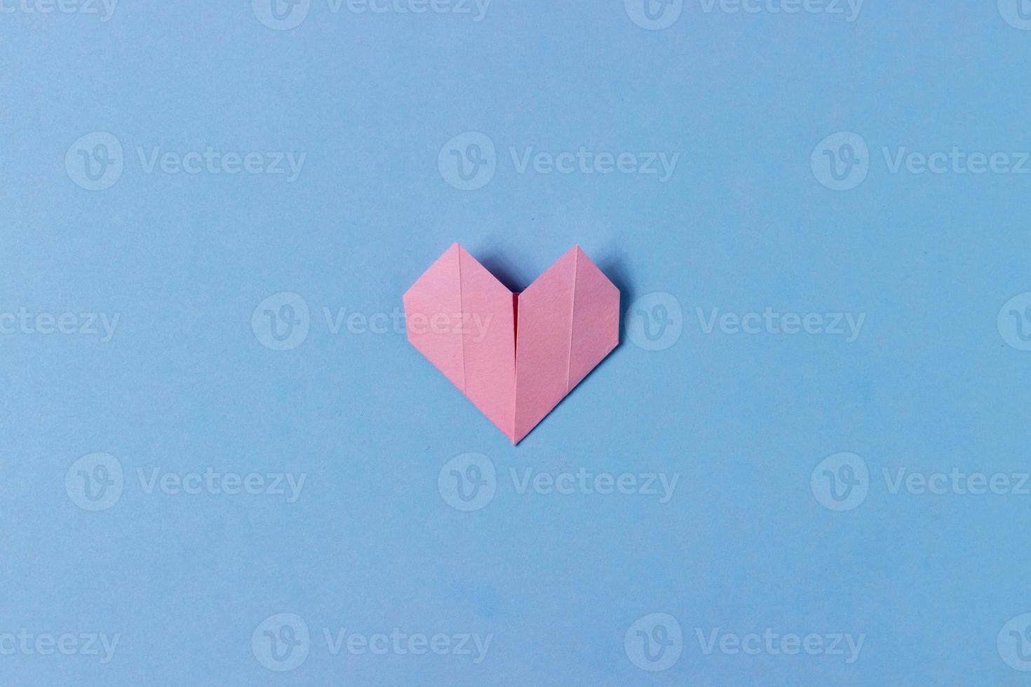 Heart folded of pink paper in origami technique on a blue background. One object. Concept of love, celebration, care, health, life photo