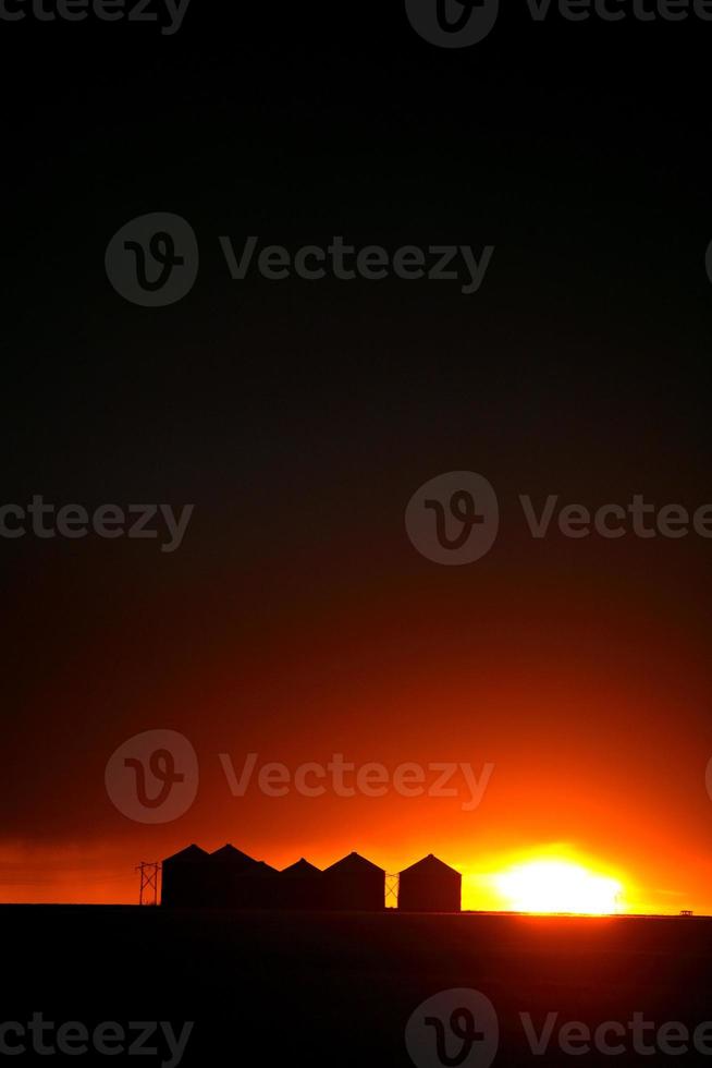 puesta de sol detrás de graneros de metal en saskatchewan foto