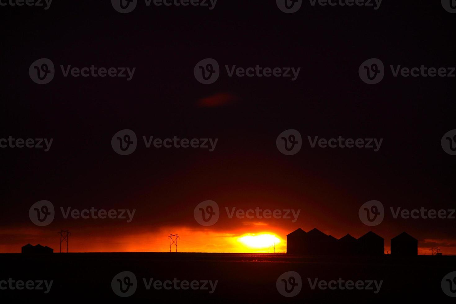 Sun setting behind metal granaries in Saskatchewan photo