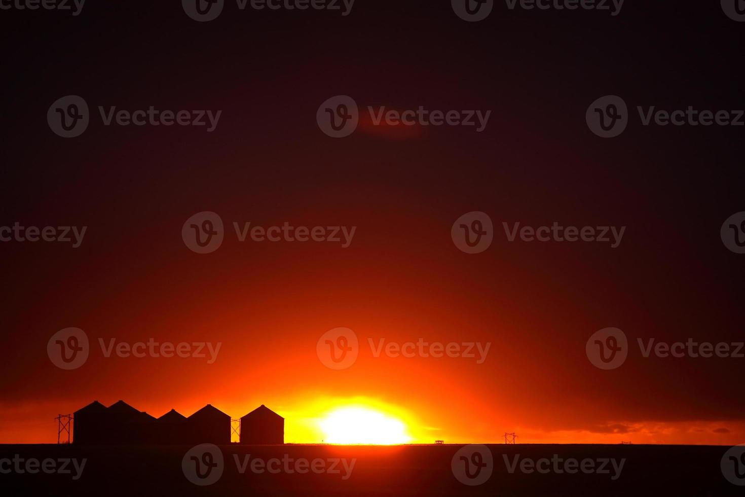 Sun setting behind metal granaries in Saskatchewan photo