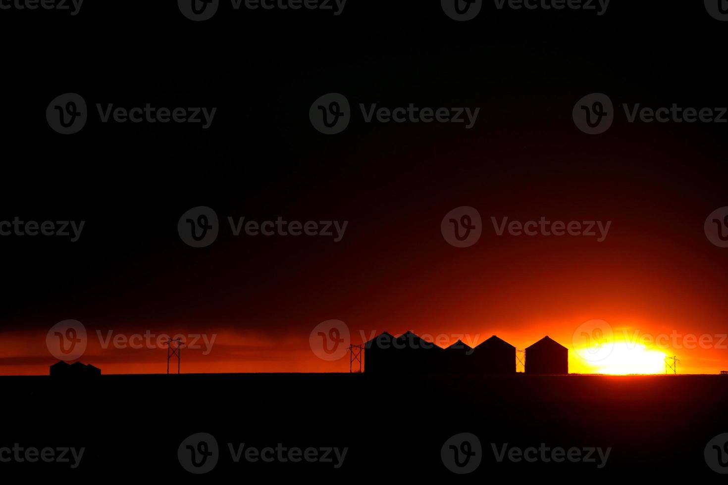 Sun setting behind metal granaries in Saskatchewan photo