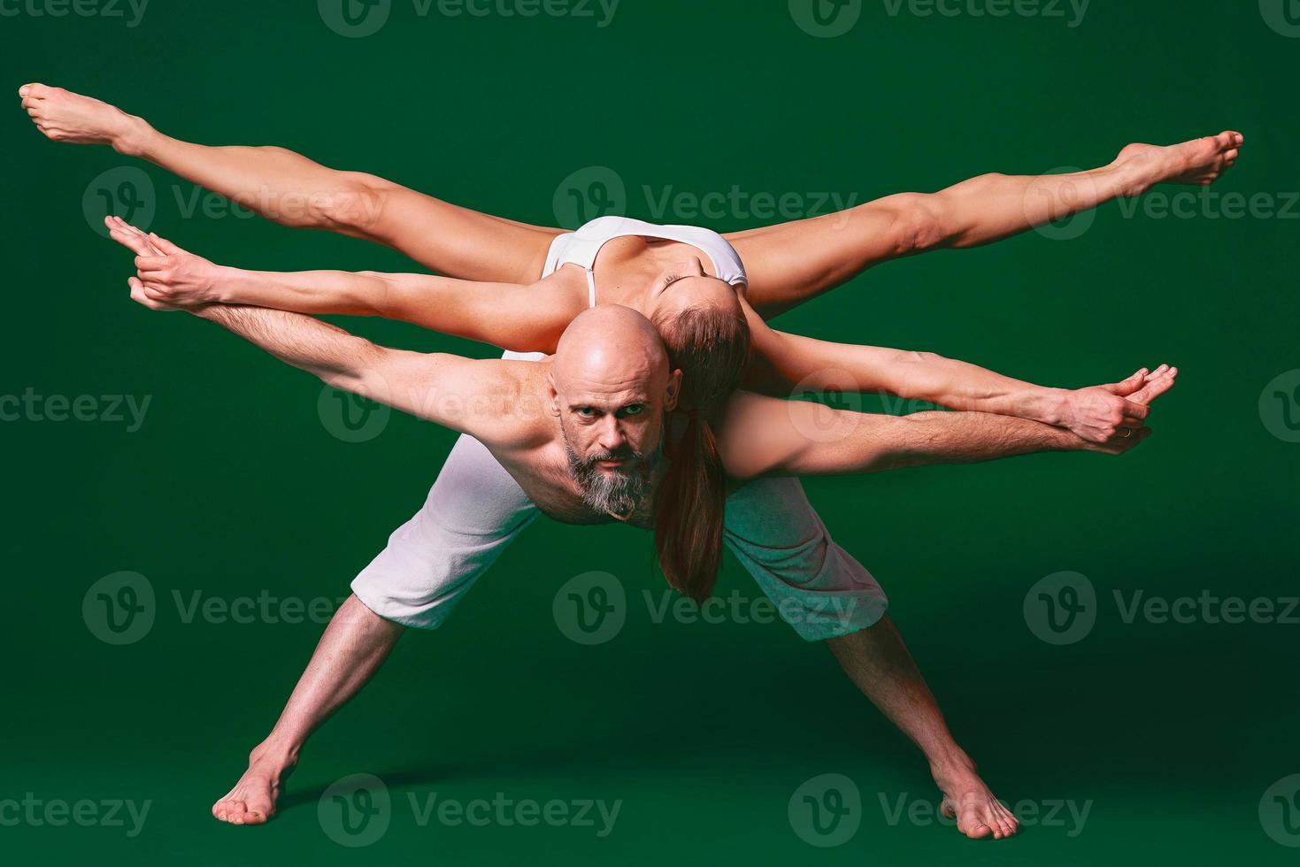 Beautiful sporty woman and man in white clothes doing yoga asanas together indoor on green background photo