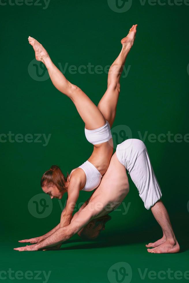 Beautiful sporty woman and man in white clothes doing yoga asanas together indoor on green background photo