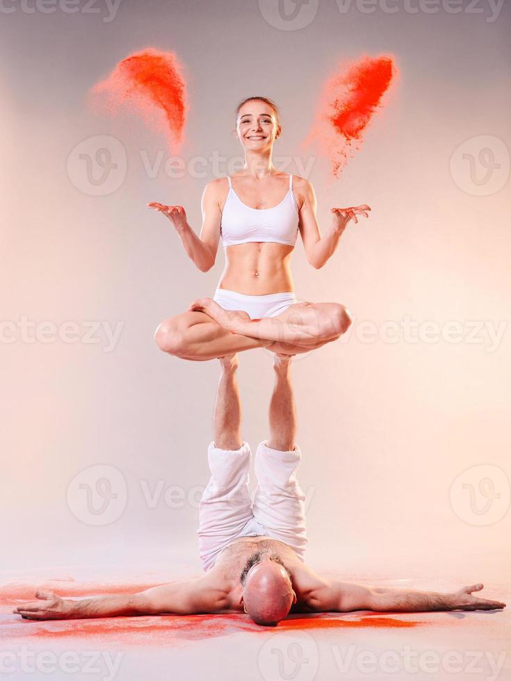 Beautiful sporty woman and man in white clothes doing yoga asanas together with colorful sand indoor photo