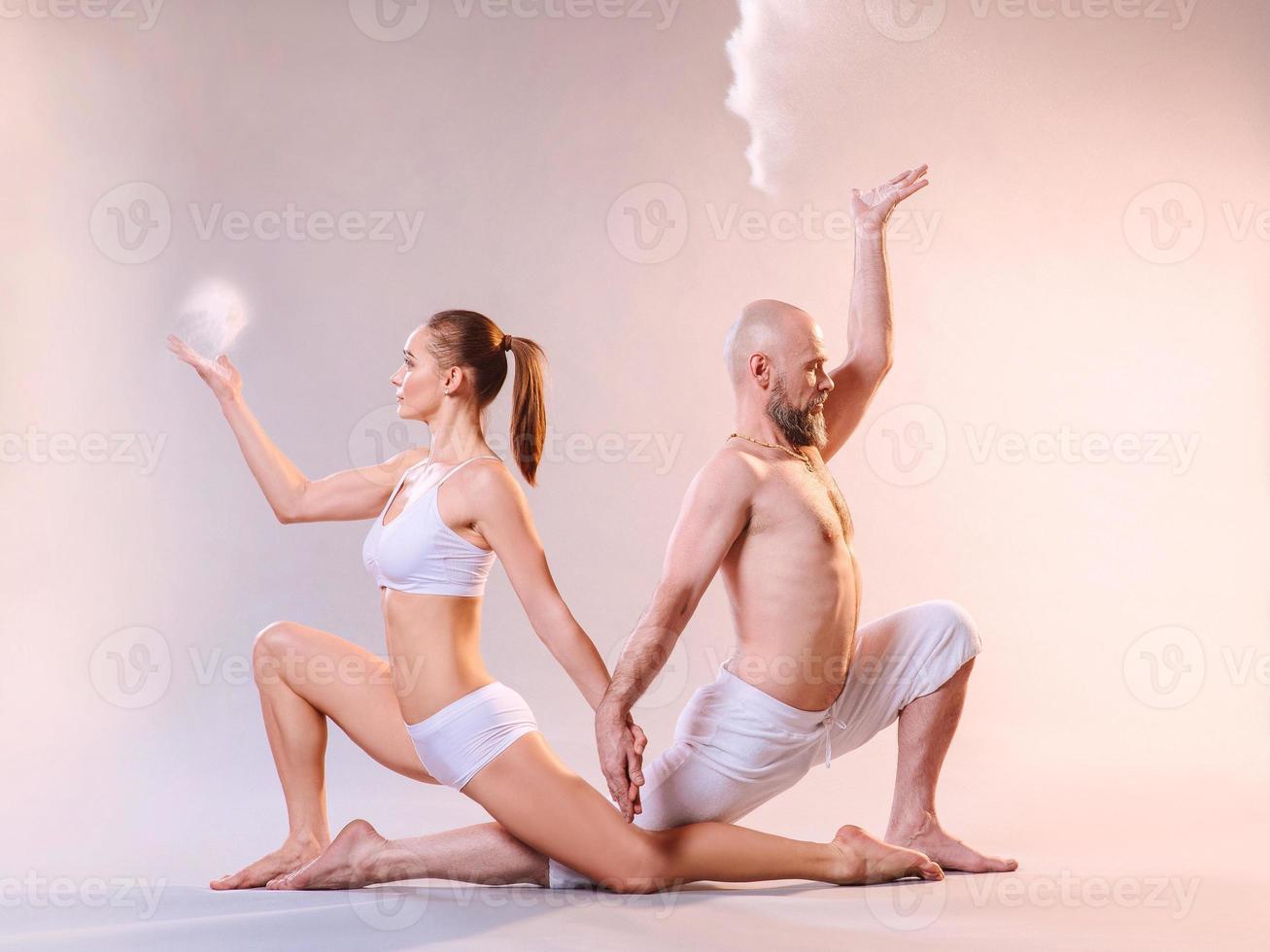 Beautiful sporty woman and man in white clothes doing yoga asanas together with colorful sand indoor photo