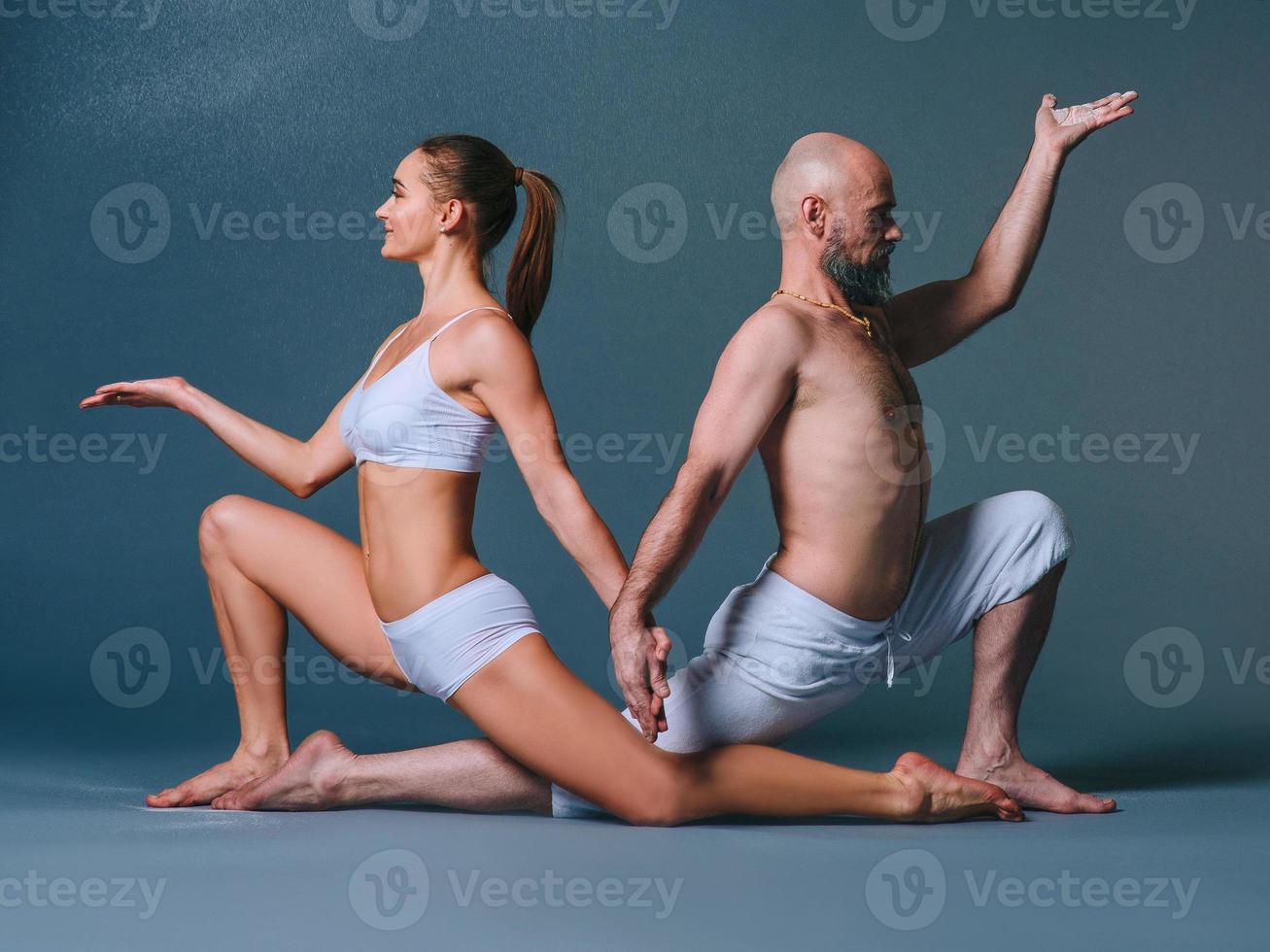 Beautiful sporty woman and man in white clothes doing yoga asanas together with colorful sand indoor photo