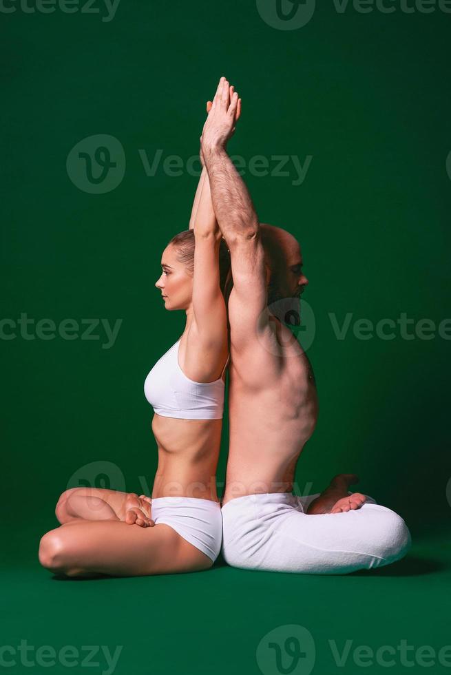 hermosa mujer deportiva y hombre con ropa blanca haciendo asanas de yoga juntos en interiores con fondo verde foto