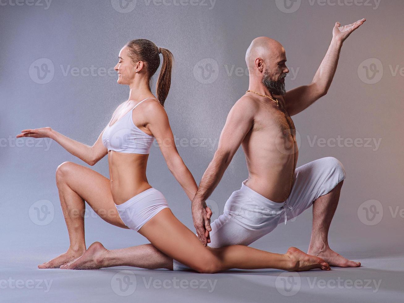 bella mujer deportiva y hombre vestido de blanco haciendo asanas de yoga junto con arena colorida en el interior foto