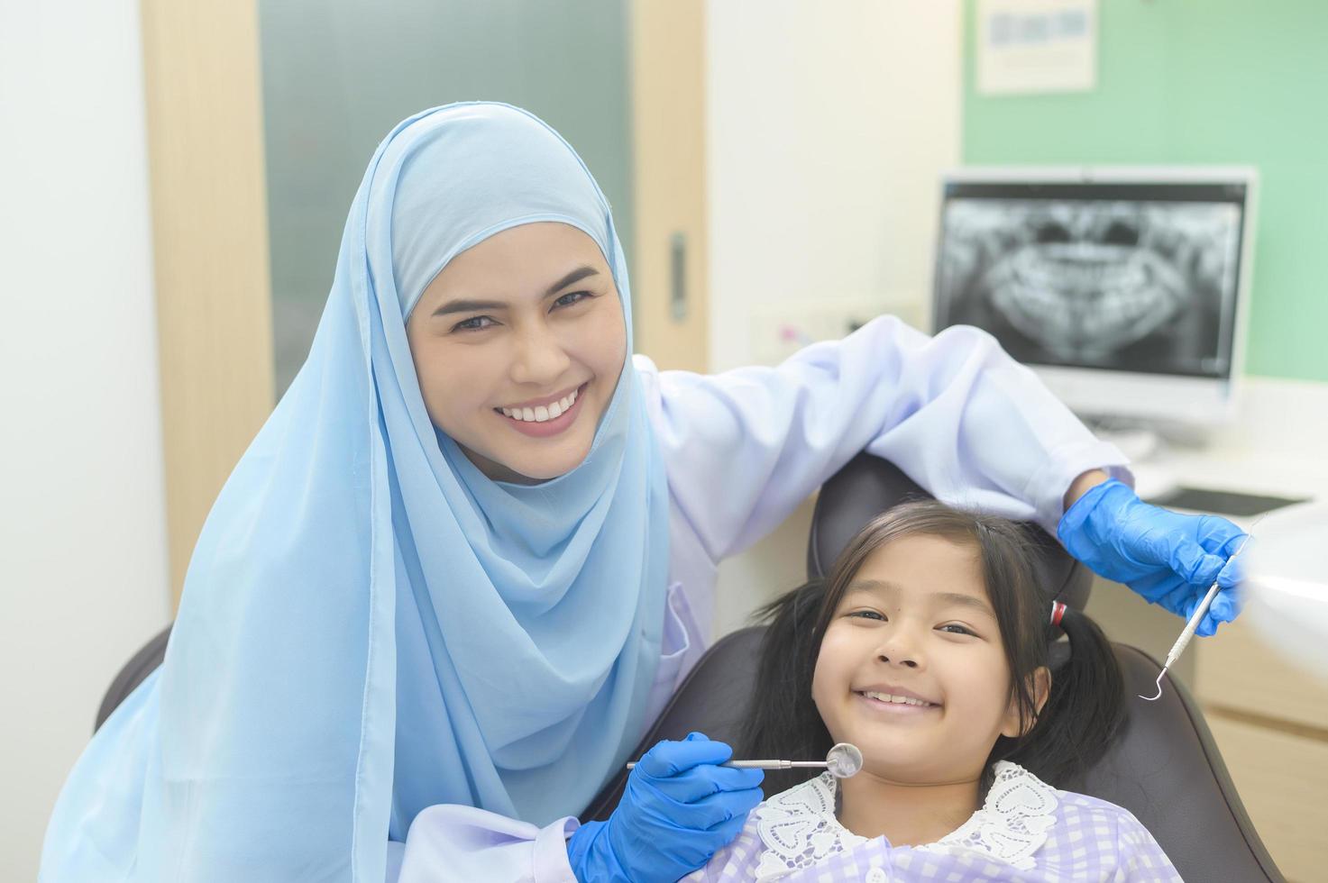 una niña linda con los dientes examinados por un dentista musulmán en la clínica dental, revisión de dientes y concepto de dientes sanos foto