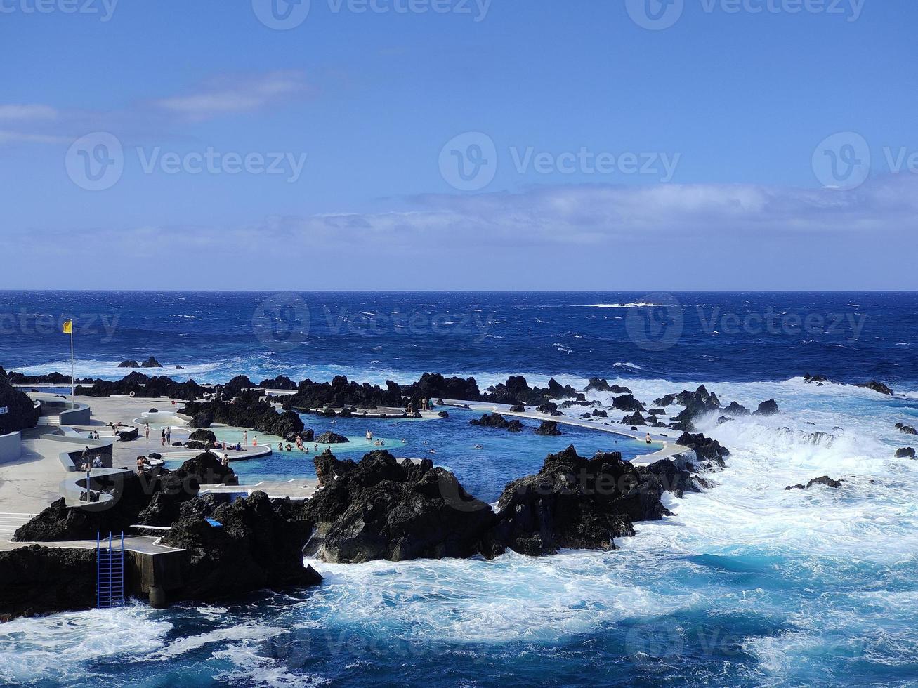 piscinas naturales en medio del océano atlántico en porto moniz, isla de madeira, portugal. tiempos de vacaciones increíbles. nubes con sol. océano y olas golpeando las rocas. gente en el agua. foto