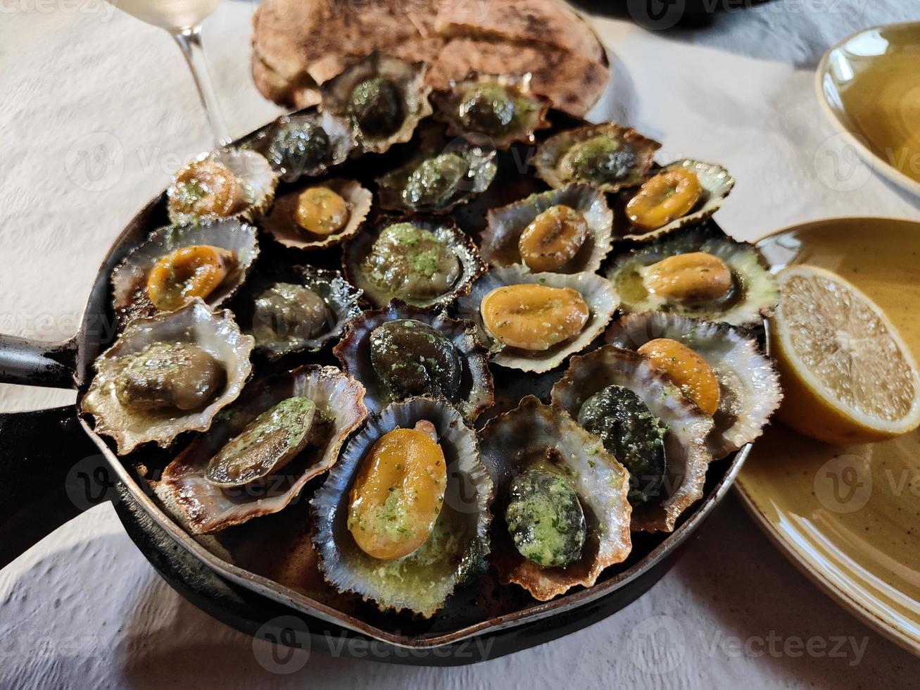 Closeup of tasty limpets with butter sauce served on the hot pan, just freshly made. Lemon on the side. Seafood. Traditional limpets, lapas from Madeira Island, Portugal. Enjoy the food. photo