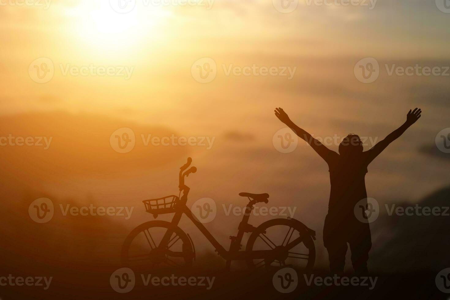 la silueta del hombre levantó la mano con una bicicleta contra el fondo de la puesta de sol. foto