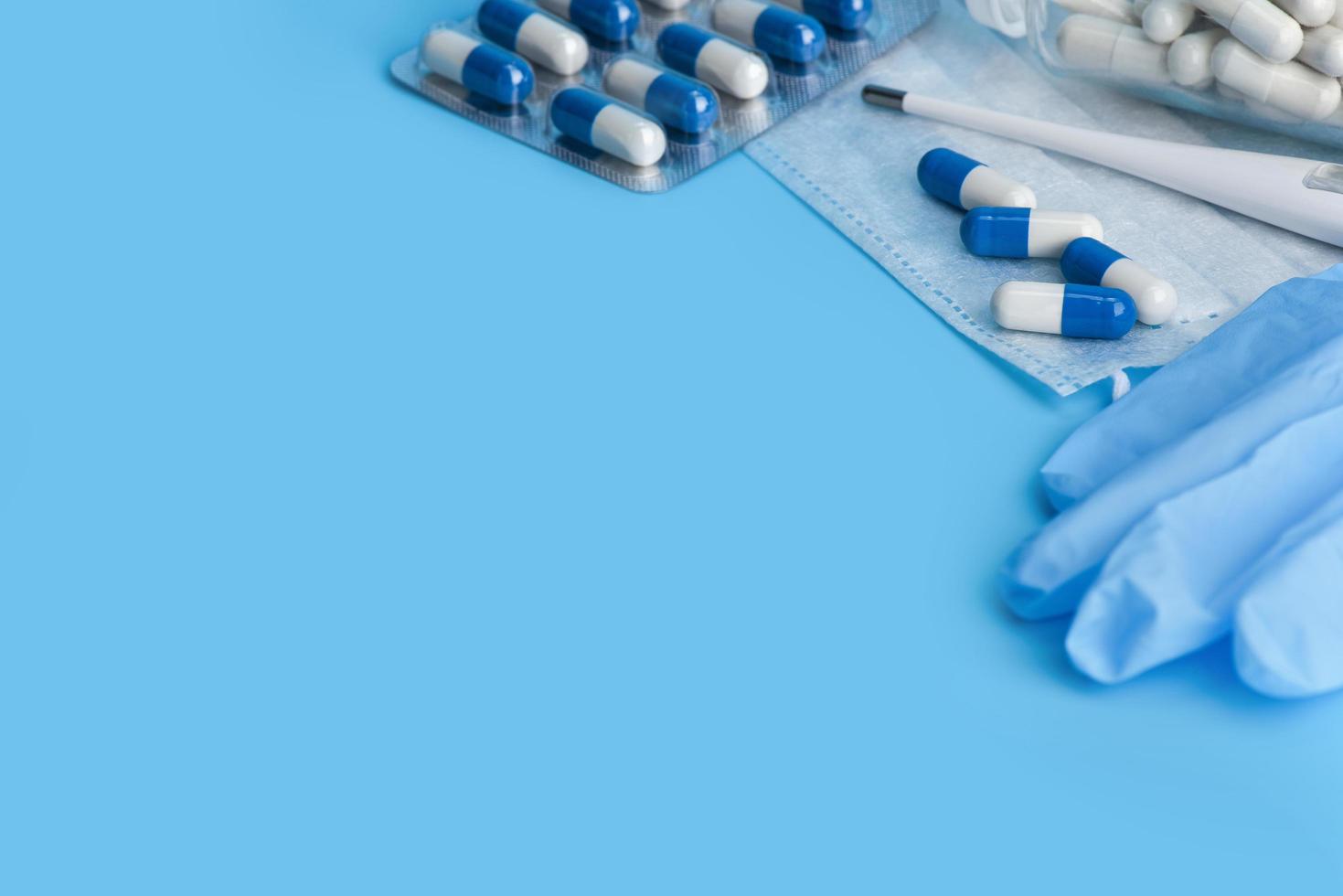 Mask, pills and medicine gloves on blue background with copy space. photo