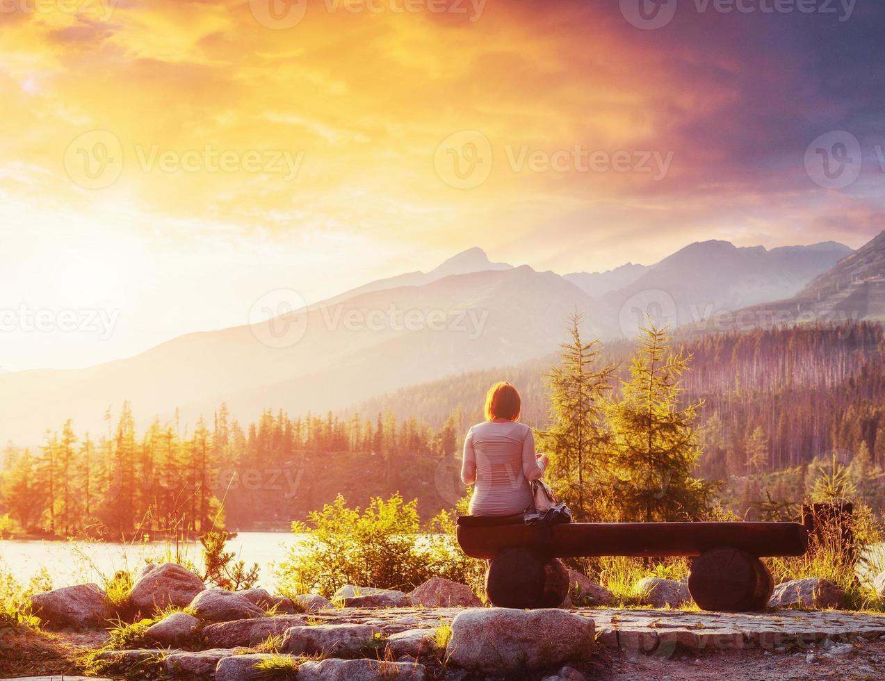 Lake Strbske pleso in High Tatras mountain, Slovakia, Europe. The girl sits on a bench and looks into the fairy-tale sky photo