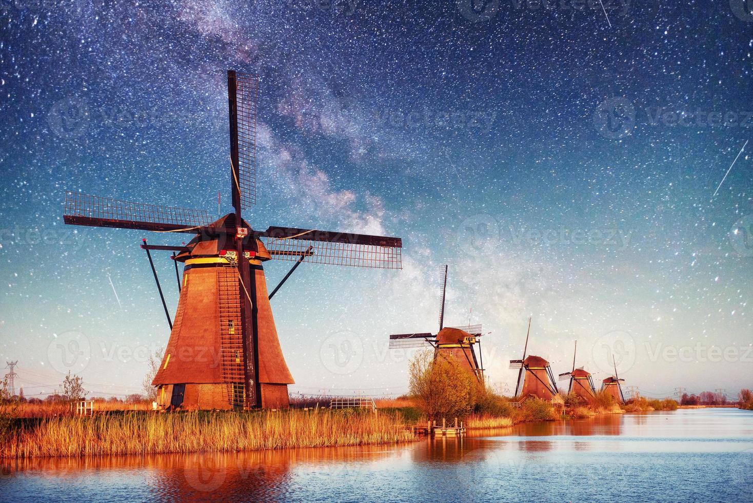 colorida noche de primavera con el tradicional canal holandés de molinos de viento en rotterdam. muelle de madera cerca de la orilla del lago. Holanda. Países Bajos. fantástico cielo estrellado y la vía láctea foto