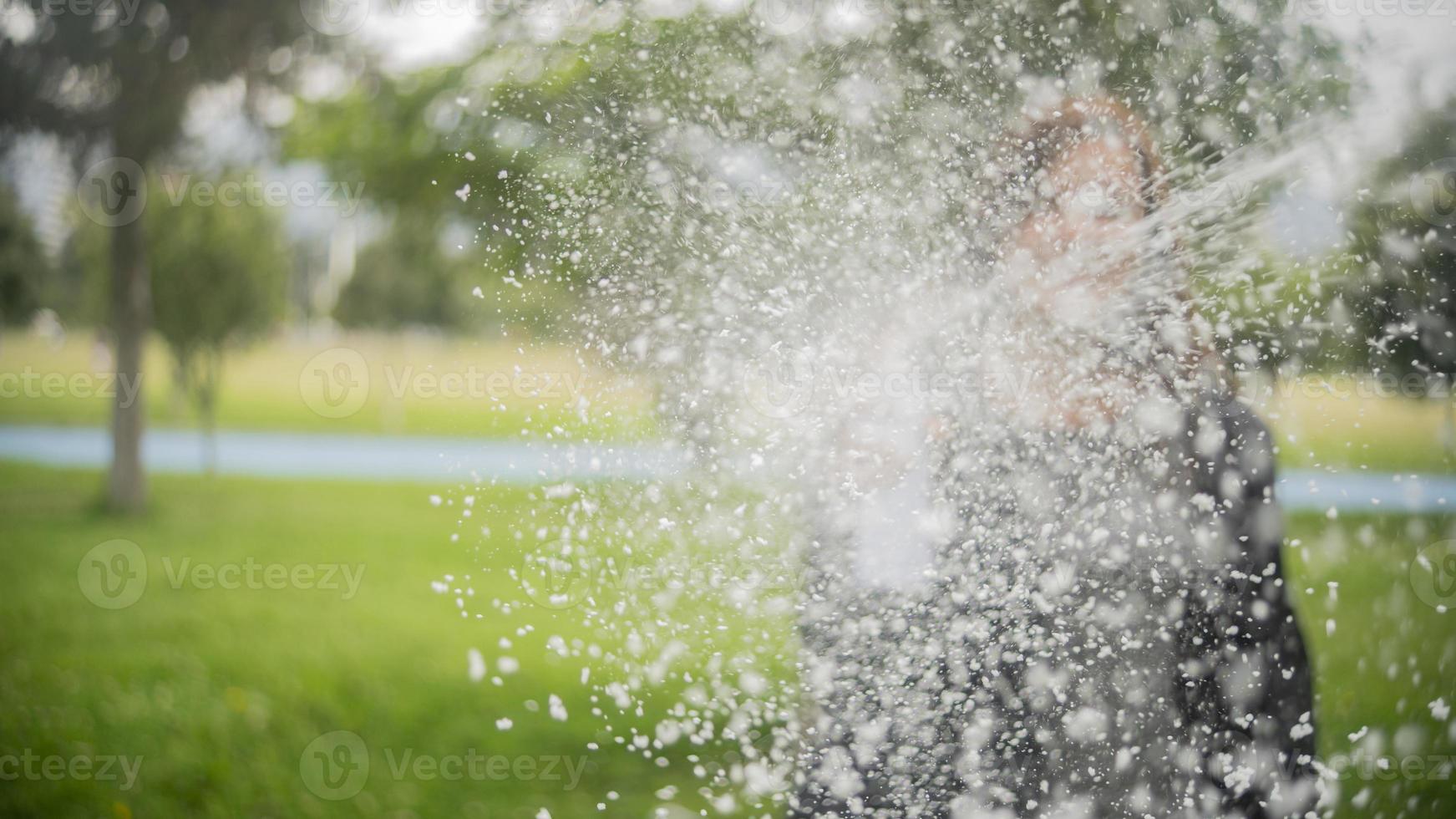 mujer hispana disparando un chorro de espuma blanca de una lata de aerosol en medio de un parque foto