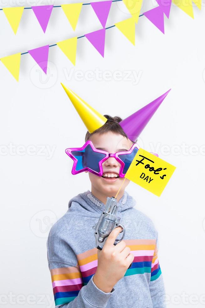 April 1st celebration concept. April Fool's day inscription on a flag from a pistol. Cheerful boy in a funny outfit photo