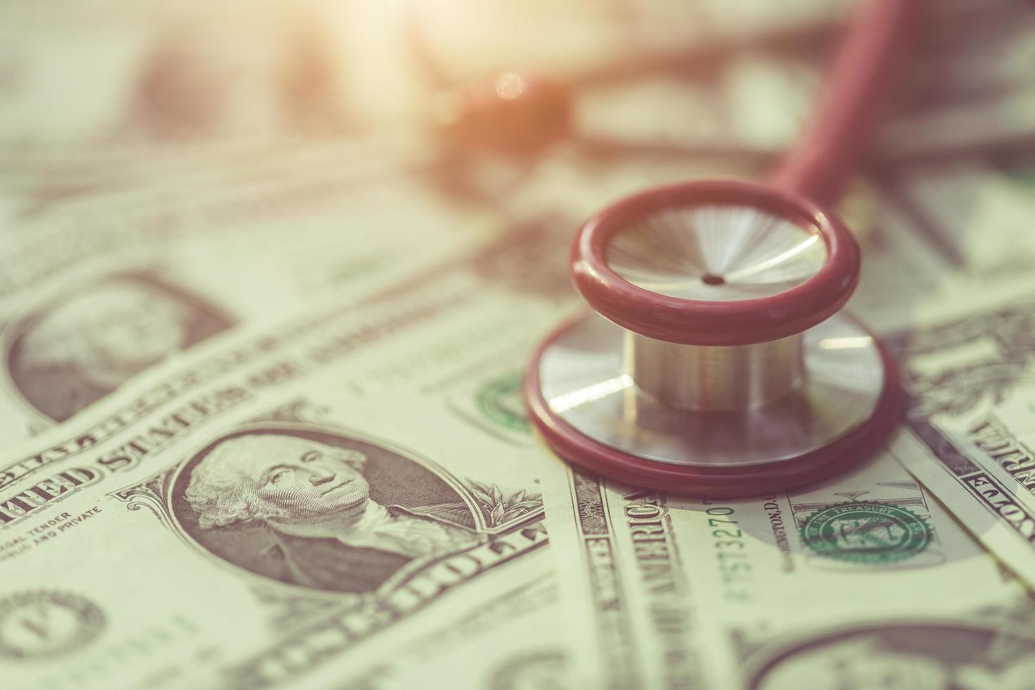 Red stethoscope on the US dollar banknote on wooden table. Health check or money and financial concept photo