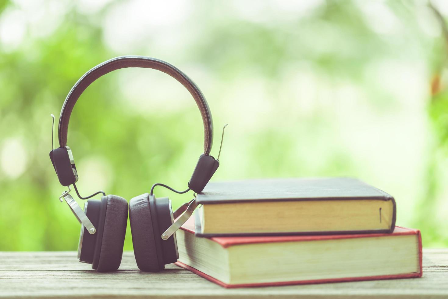 Book and black headphone on wooden table with abstract green nature blur background. Reading and education concept photo