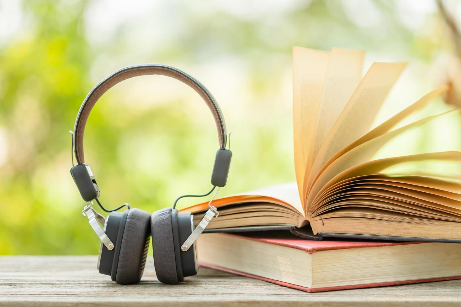 Book and black headphone on wooden table with abstract green nature blur background. Reading and education concept photo