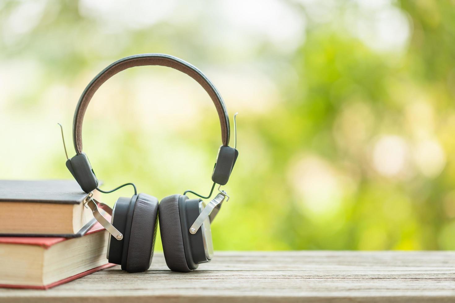 Book and black headphone on wooden table with abstract green nature blur background. Reading and education concept photo
