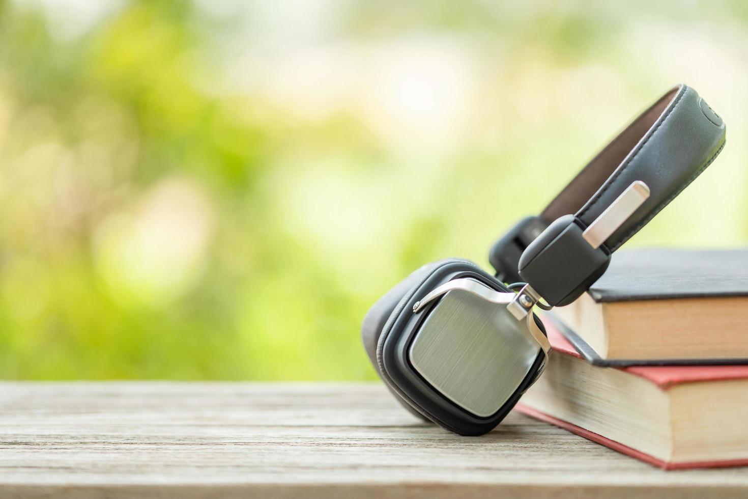 Book and black headphone on wooden table with abstract green nature blur background. Reading and education concept photo