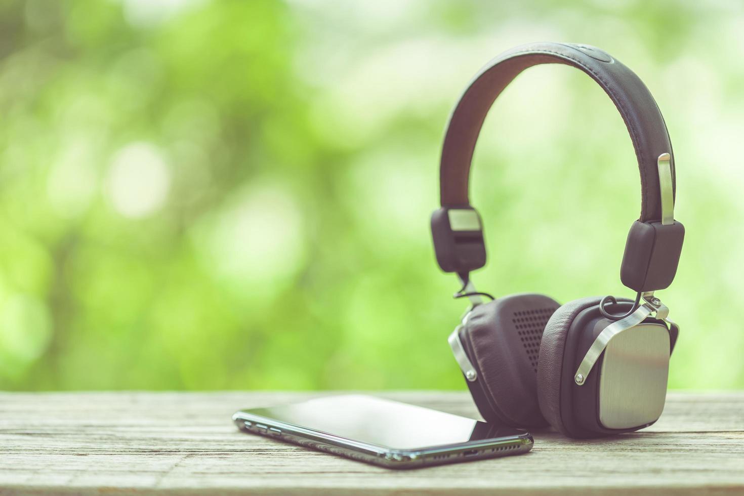 nuevo teléfono inteligente y auriculares en una mesa de madera con espacio verde naturaleza desenfoque de fondo foto