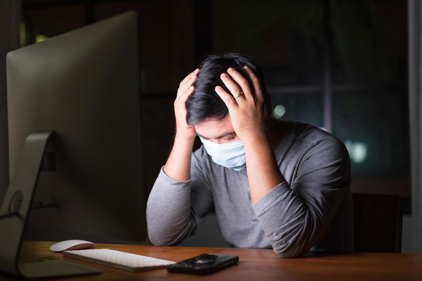 hombre con mascarilla preventiva y trabajando desde casa por la noche en situación de enfermedad por el virus de la corona. trabajo desde casa y concepto saludable foto