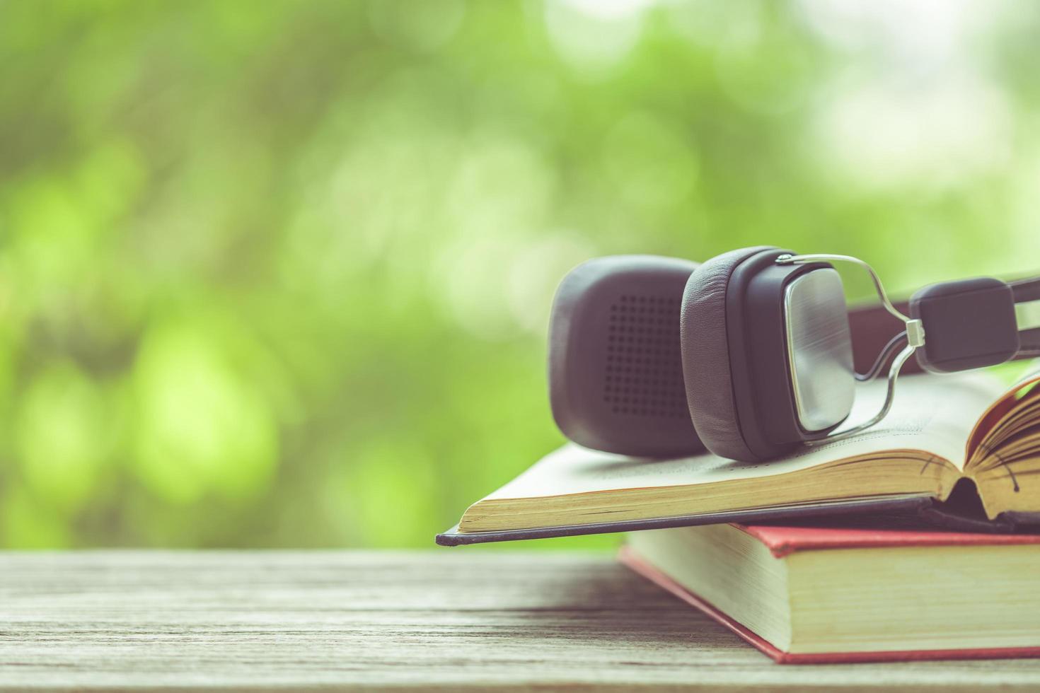 Book and black headphone on wooden table with abstract green nature blur background. Reading and education concept photo