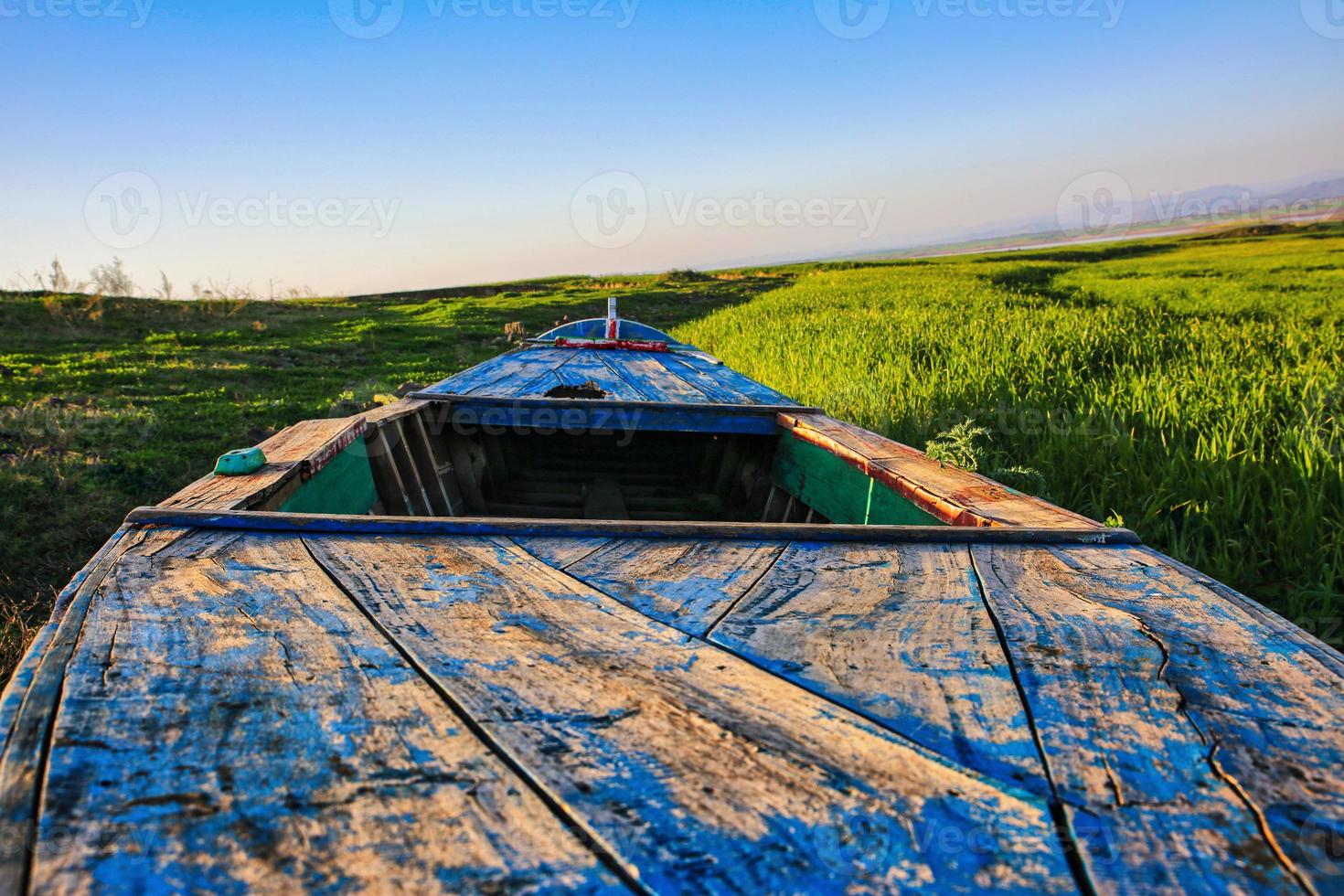 An old wooden boatwreck, showing signs of decay and deterioration. An old nauitical sea vessel grounded on the shore with rusty rotten ruins. Nature and the grass taking its toll on old boats. photo