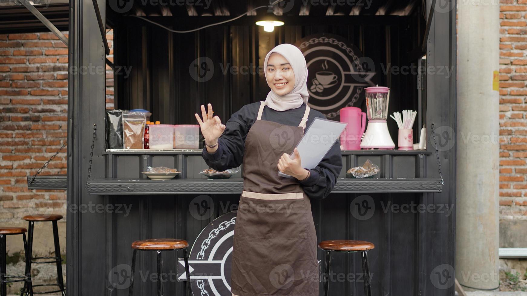 hermosa camarera asiática trae la lista del menú haciendo un gesto de ok en el contenedor de la cabina del café foto