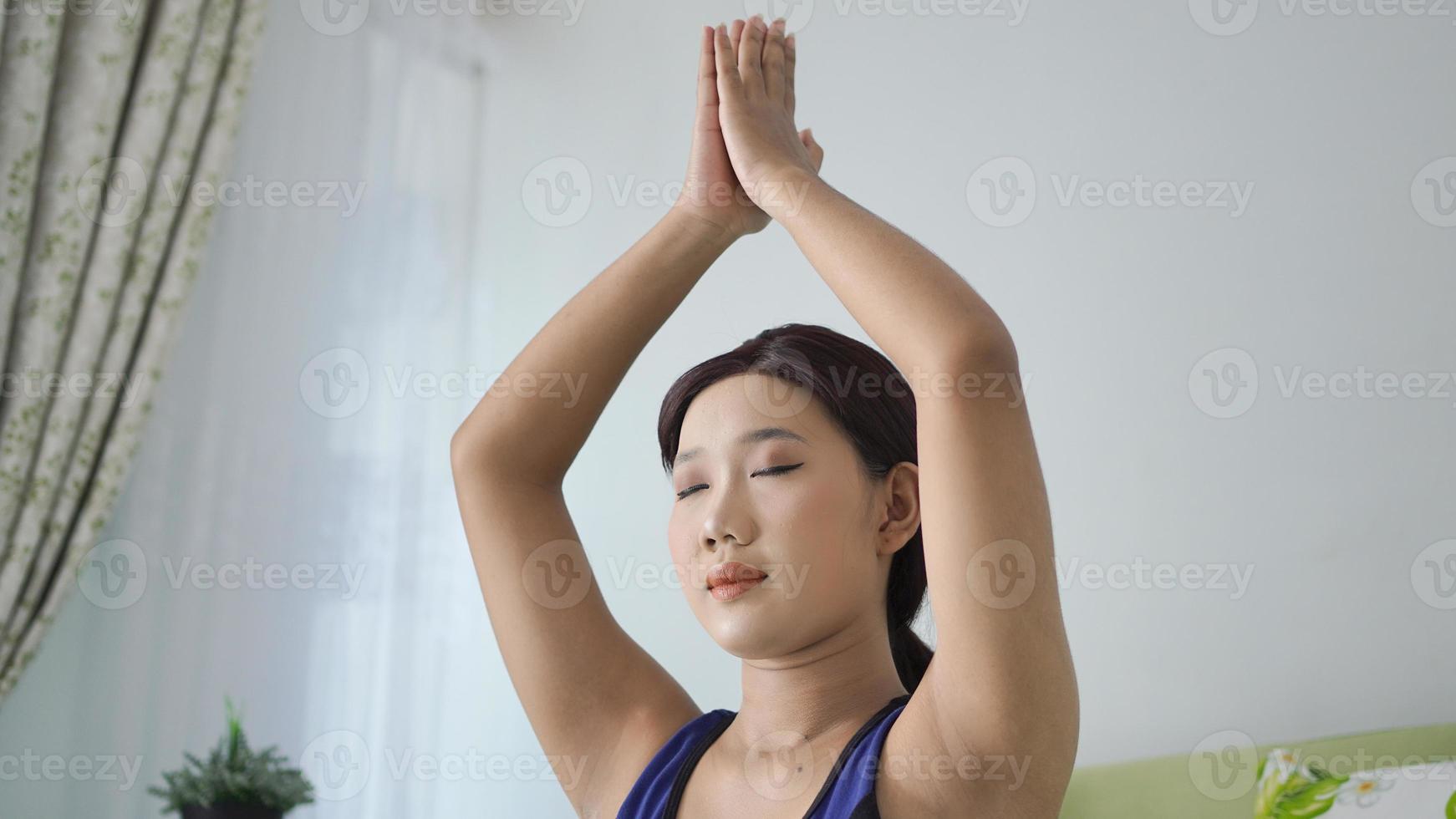 mujer asiática practicando yoga en casa haciendo movimiento manual foto